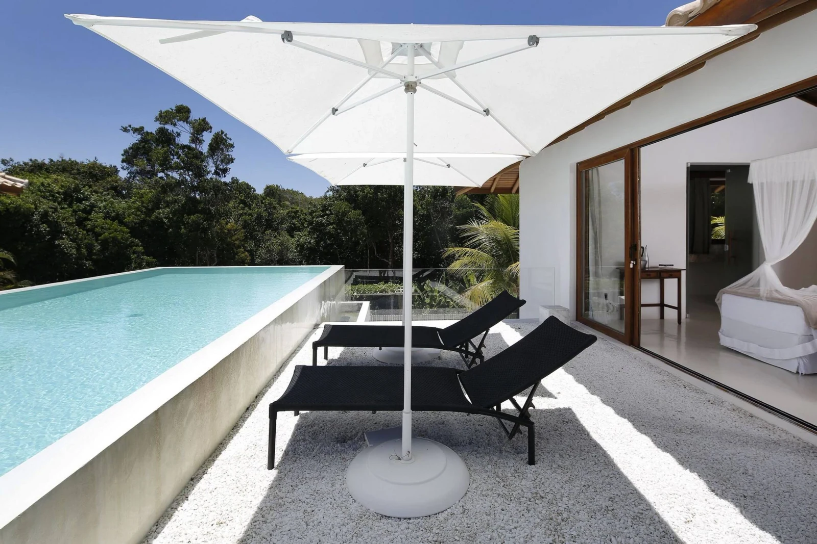 Deck da piscina com guarda-sol e espreguiçadeiras, mansão de luxo em Trancoso
